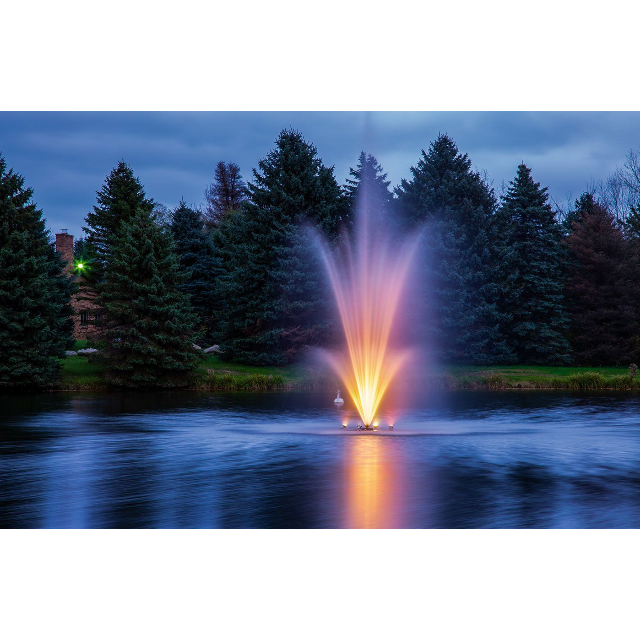 Scott Aerator Amherst Fountain lighted by warm white lights in a large pond surrounded by trees at night
